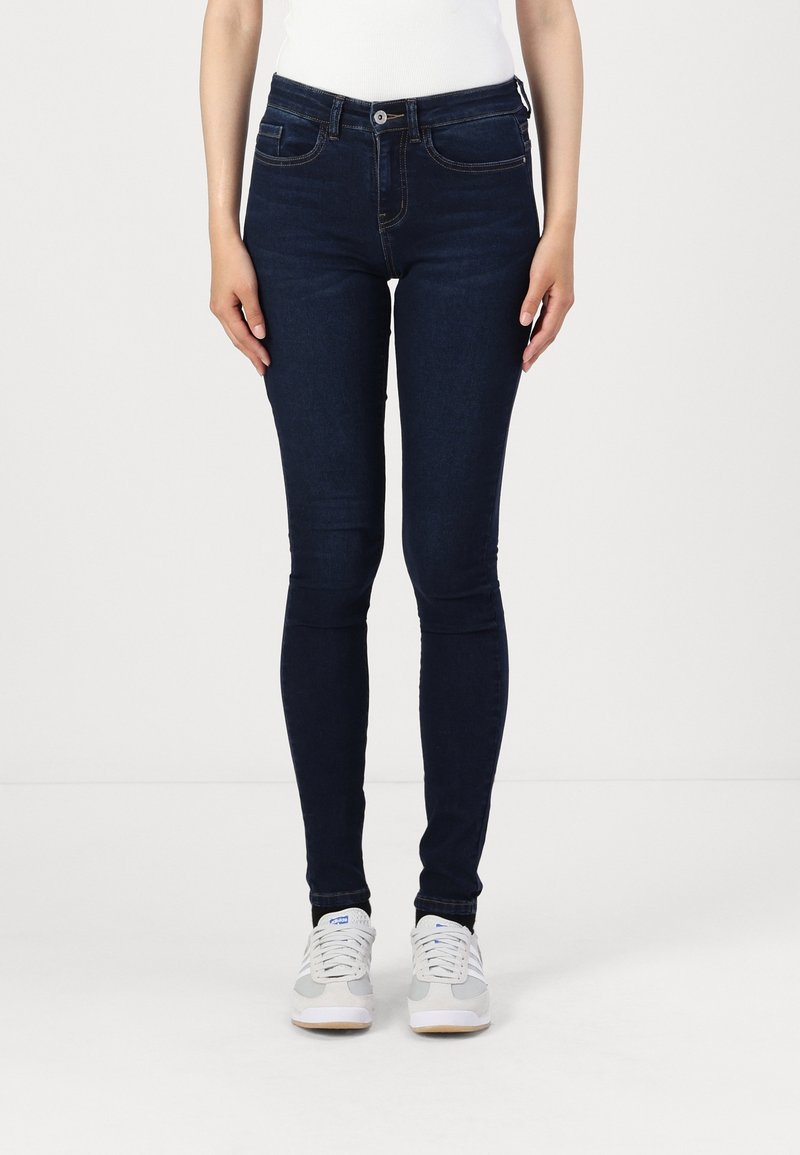 Dark blue skinny jeans with a smooth texture, five pockets, and slight fading on the thighs. Paired with white sneakers.