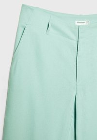 Pantalons vert menthe en tissu doux, avec une coupe droite, deux poches avant et un pli subtil sur le devant.