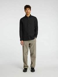 Camisa de lino negra con un diseño de botones, combinada con pantalones beige y zapatos negros. La tela parece suave y ligera.