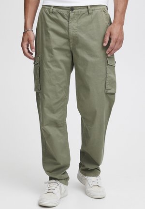 Cargo-Hosen aus olivgrünem Stoff, mit mehreren Seitentaschen, einem lässigen Schnitt und geradem Bein. Kombiniert mit weißen Sneakers.