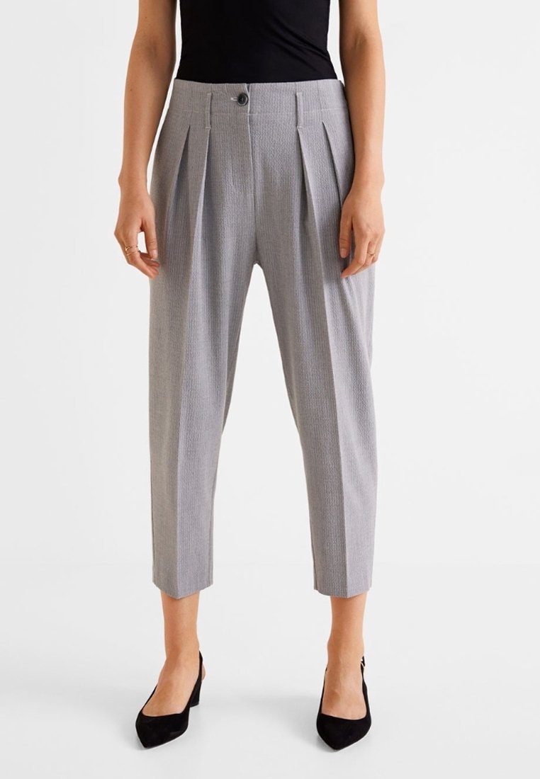 Femme portant un pantalon court plissé gris taille haute associé à des talons noirs à bout pointu et un top noir sans manches.