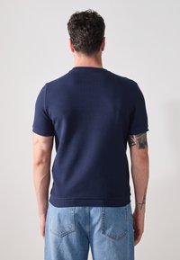 Marineblå kortermet, teksturert t-skjorte med rund hals og ribbestrikket stoff, brukt sammen med lyseblå denimjeans.