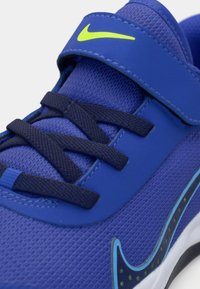 Zapatilla azul con parte superior de malla, lengüeta acolchada y cordones en color marino. Presenta un swoosh de color verde neón y acentos texturizados a lo largo del costado.
