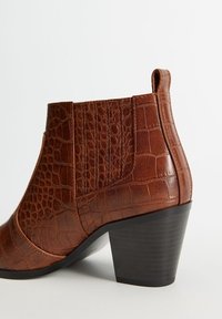 Bottine en cuir marron avec texture crocodile, empiècement latéral élastique, languette de tirage et talon bloc empilé noir.