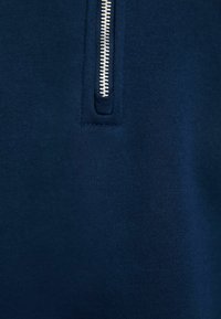 Suéter de cuello con cremallera en azul marino, hecho de una tela suave, con una cremallera de metal plateado y un tirador texturizado, además de un acabado suave.