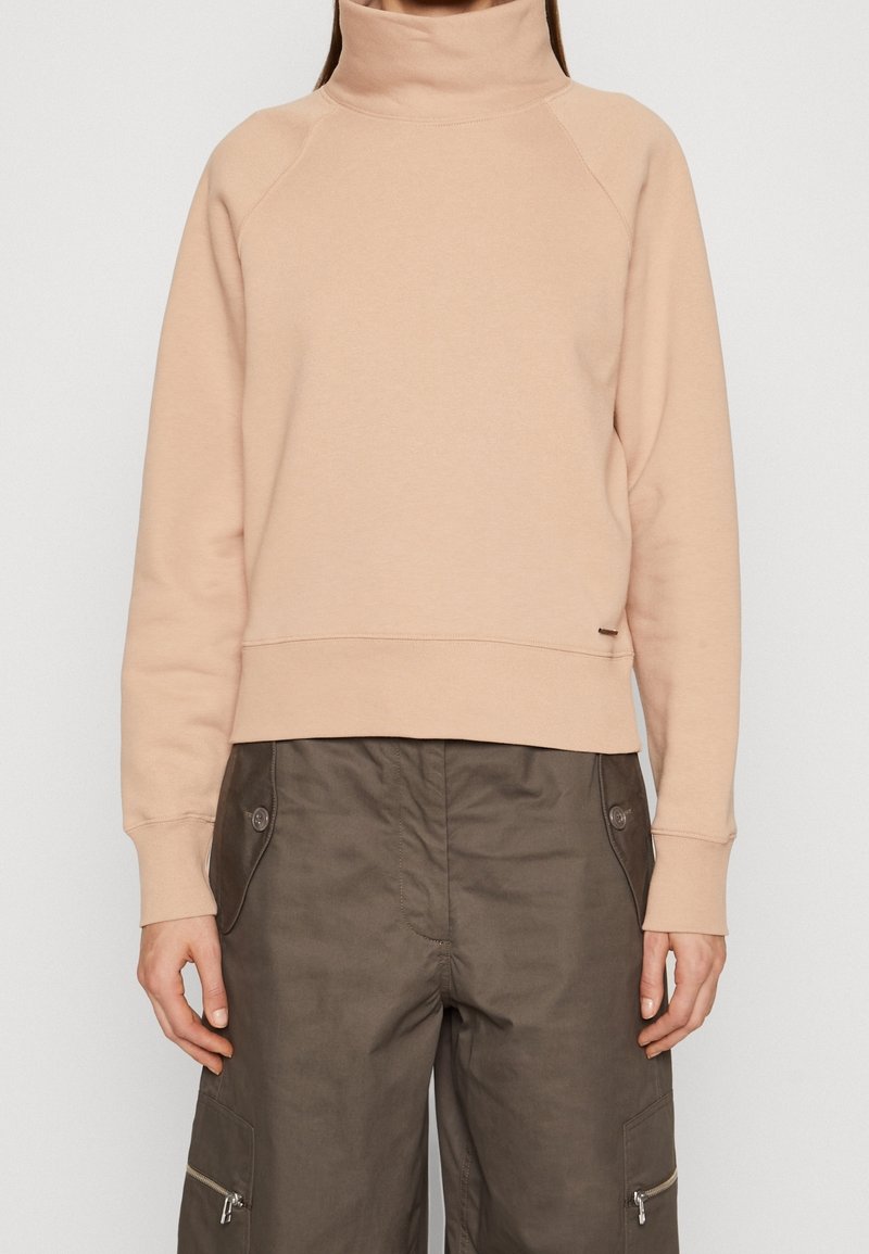 Sudadera color melocotón con cuello alto, puños acanalados y dobladillo recortado. Textura suave y diseño minimalista. Combinada con pantalones cargo.