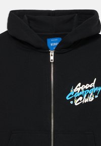 Sort zip-up hoodie med frontlommer, sølv lynlås og teksten "Good Company Club" i hvid og blå med små ild- og hjertegrafikker.