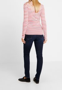 Röd och vit randig långärmad skjorta, figursydd design, kombinerad med mörkblå denimjeans och svarta slip-on skor. Enfärgad bakgrund.