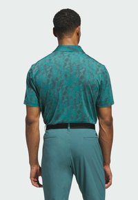Short-sleeve polo shirt in teal with a textured pattern, featuring a collar and a back design. Worn with matching teal pants, visible waistband.