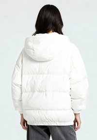 Giacca a vento bianca con cappuccio, caratterizzata da una texture trapuntata, polsini elastici e una vestibilità leggermente oversize.