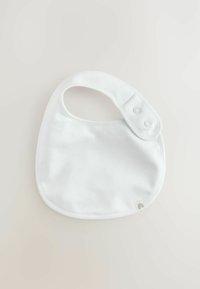 White cotton bib with a rounded shape, featuring a snap closure and smooth texture. Notable detail includes a small logo in the corner.