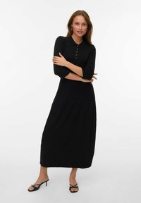 Abito nero a maniche lunghe con colletto, dettagli con bottoni e corpino aderente, che si allunga in una gonna ampia fino alla caviglia. Design casual.