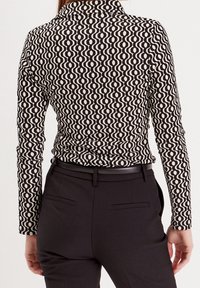 Haut noir et blanc à manches longues avec un motif de vagues, associé à un pantalon noir ajusté. Le haut présente un col discret et une coupe près du corps.