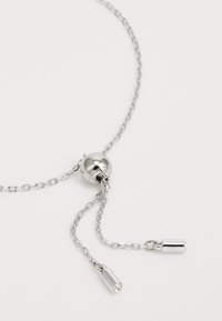 Collier en argent avec un design en chaîne, un pendentif en forme de boule ronde et deux accents cylindriques suspendus. Texture lisse et finition réfléchissante.