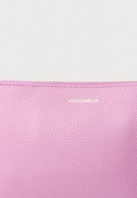 Roosa tekstuuriga nahast rahakott luku-äärse tõmblukuga, millel on kuldne, reljeefne logo "Coccinelle" peal. Minimalistlik disain.