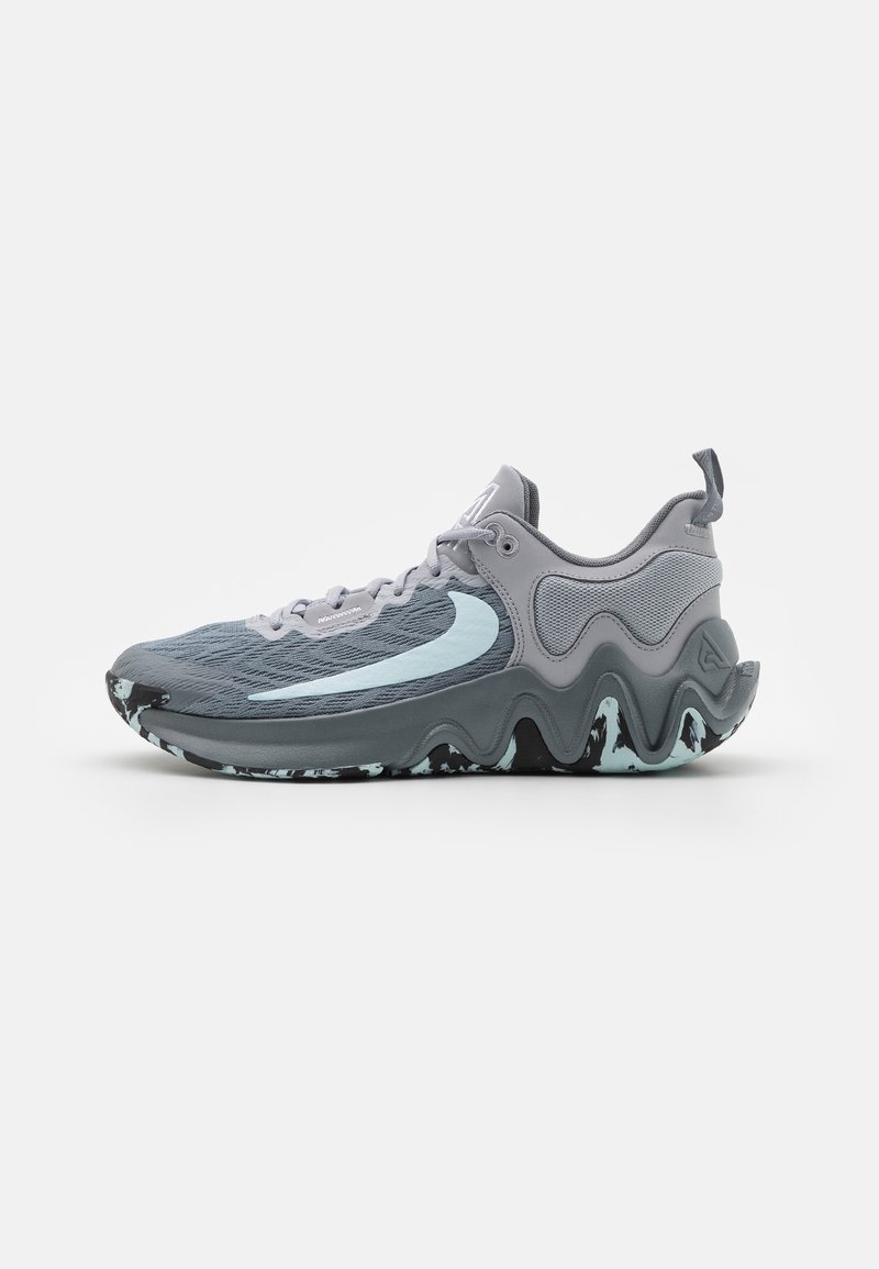 Chaussure de sport grise avec un swoosh bleu clair, semelle à motif ondulé, dessus en mesh et languette au talon, vue de côté.