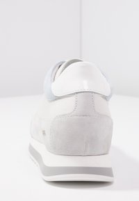 Ljusgrå sneaker med mocka och släta lädermaterial. Rund häl med en glansig vit accent och en kontrasterande texturerad bakpanel.