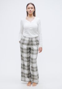 Λευκή μακρυμάνικη μπλούζα henley με πατιλέτα κουμπιών, συνδυασμένη με φαρδιά παντελόνια σε πράσινο και λευκό καρό. Ομαλό ύφασμα, άνετη εφαρμογή.