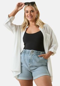 Valkoinen pitkähihainen paita mustan topin päällä, yhdistettynä vaaleansinisiin farkkushortseihin, joissa on joustava vyötärö ja käännetyt hihan päädyt.