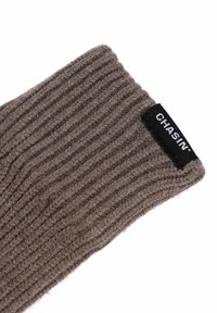 Gant en laine marron tricoté avec une texture côtelée. Étiquette noire avec le logo "CHASIN'" au niveau du poignet. Gros plan sur le tissu et la couture.