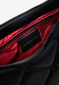 Black quilted leather clutch with a red satin interior and a black label. Features a zipper closure and a smooth texture.