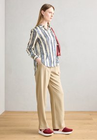 Blouse rayée en crème, bleu et noir avec des manches longues, pantalon large beige et baskets rouges avec semelles et accents blancs.