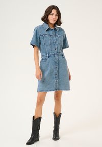 Helesinim vest, helesinises tooni, lühikeste varrukatega, nööbiga ees, kahe rinnataskuga ja taskutega puusadel. Kantud mustade cowboy saapadega.