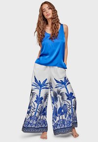 Blue satin tank top paired with wide-leg white pants featuring a blue tropical print. Pants have a decorative bottom hem. Soft texture.