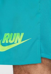 Shorts deportivos turquesas con un panel lateral de malla transpirable, que cuentan con un logo "RUN" en verde neón y un gráfico del swoosh de Nike.