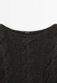 Pull en maille gris foncé avec un motif torsadé, col rond, et étiquette visible. Fabriqué avec un fil texturé pour la chaleur et le confort.
