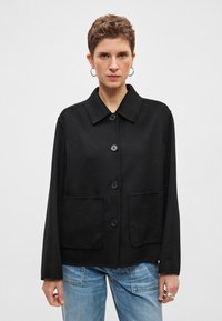 Casaco de mistura de lã preta com gola de colarinho, fecho frontal de botões, dois bolsos grandes e mangas compridas largas.