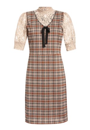 Kobieta ubrana w brązową, kraciastą sukienkę do kolan z czarną kokardą oraz beżowy koronkowy top o długości do łokcia, zestawione z beżowymi sandałami na koturnie z paskiem wokół kostki.