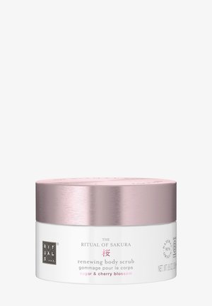 Behälter des The Ritual of Sakura erneuernden Körperscrubs mit rosa metallischem Deckel und weißem Etikett, das Zucker- und Kirschblütenduft zeigt.