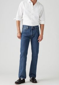 Vaqueros de mezclilla azul claro con un corte de pierna recta, combinados con una camisa blanca de botones. Los vaqueros cuentan con cinco bolsillos y trabillas para cinturón.