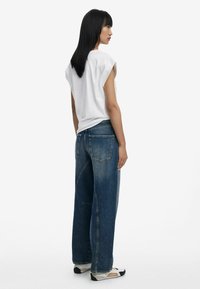 Weißes übergroßes T-Shirt mit Kapellärmeln, kombiniert mit lockeren blauen Jeans aus Denim mit verblichener Waschung und auffälligen Nähten.