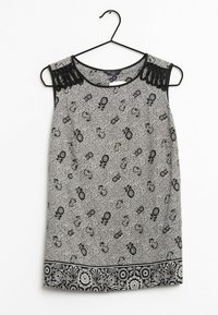 Blusa senza maniche con motivo floreale bianco e nero e dettagli in pizzo sulle spalle, appesa a una gruccia nera su sfondo bianco.