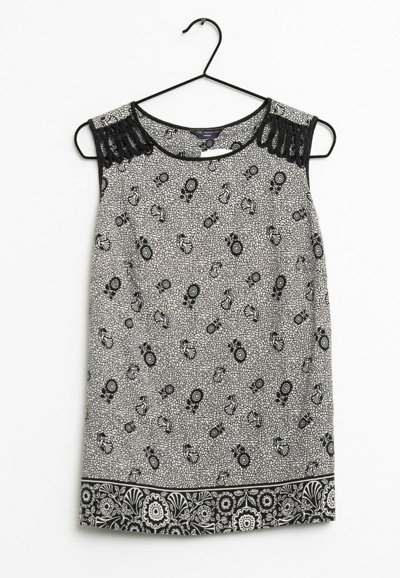 Ärmlös blus i svart och vitt med blommönster och spetsdetaljer på axlarna, hängande på en svart galge mot vit bakgrund.