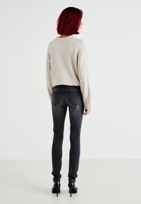 Jersey de color beige claro con mangas acanaladas, combinado con jeans skinny de color gris oscuro. Zapatos de tacón alto negros, vistos desde atrás.