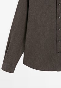 Dark brown long-sleeve button-up shirt, featuring a textured ribbed fabric, standard collar, and black buttons along the front.