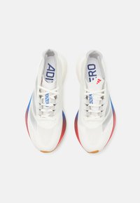 Weiße Sportschuhe mit einem atmungsaktiven Mesh-Obermaterial, das blaue und rote Farbverläufe an der Sohle aufweist und eine flache Schnürung hat.
