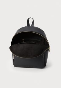 Zaino in pelle nera con interni in suede, chiusura con zip dorata e una maniglia superiore singola. Presenta una tasca frontale e un design elegante.