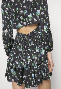Ensemble deux pièces noir à motif floral avec manches longues, taille haute smockée, jupe à volants et top court laissant entrevoir le ventre et le dos.