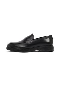 Mocasines de cuero negro con un acabado suave, punta redondeada y sutil detalle de costura. Presentan una suela de goma texturizada y baja, además de un diseño sin cordones.