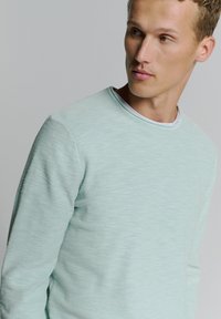 Lichtblauwe trui van zacht, textuurstof, met een ronde hals en lange mouwen met subtiel gemêleerd patroon.