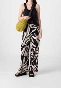 Black tank top with ruffled edges, beige and black leaf-patterned wide-leg trousers, and a textured mustard yellow bag. Flat black sandals.