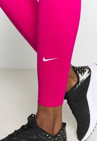 Fuksjowe legginsy wykonane z elastycznego materiału z białym logo Nike, w połączeniu z czarnymi butami do biegania z refleksyjnymi akcentami.