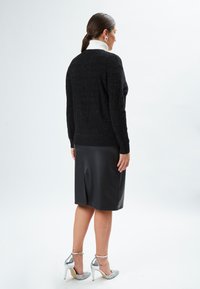 Maglione nero con riflessi metallici, abbinato a una minigonna in pelle nera aderente. Tacchi alti con cinturino alla caviglia metallici e dettagli scintillanti.