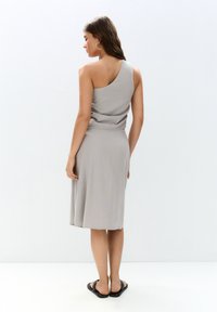 Grau, ein Schulter Kleid mit einem schwingenden, knielangen Rock. Hergestellt aus weichem Stoff, hat es eine taillierte Taille und minimale Details, kombiniert mit flachen Sandalen.