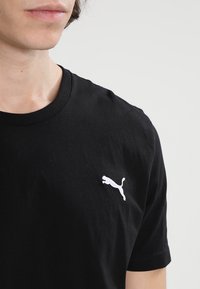 Svart bomull t-shirt med en vit broderad Puma-logotyp på vänster bröstområde, kort ärm och rundad halsringning.