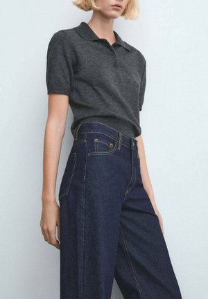 Persona rubia que lleva una camisa polo de manga corta de color gris oscuro metida en unos vaqueros de cintura alta de color azul oscuro con costuras visibles.